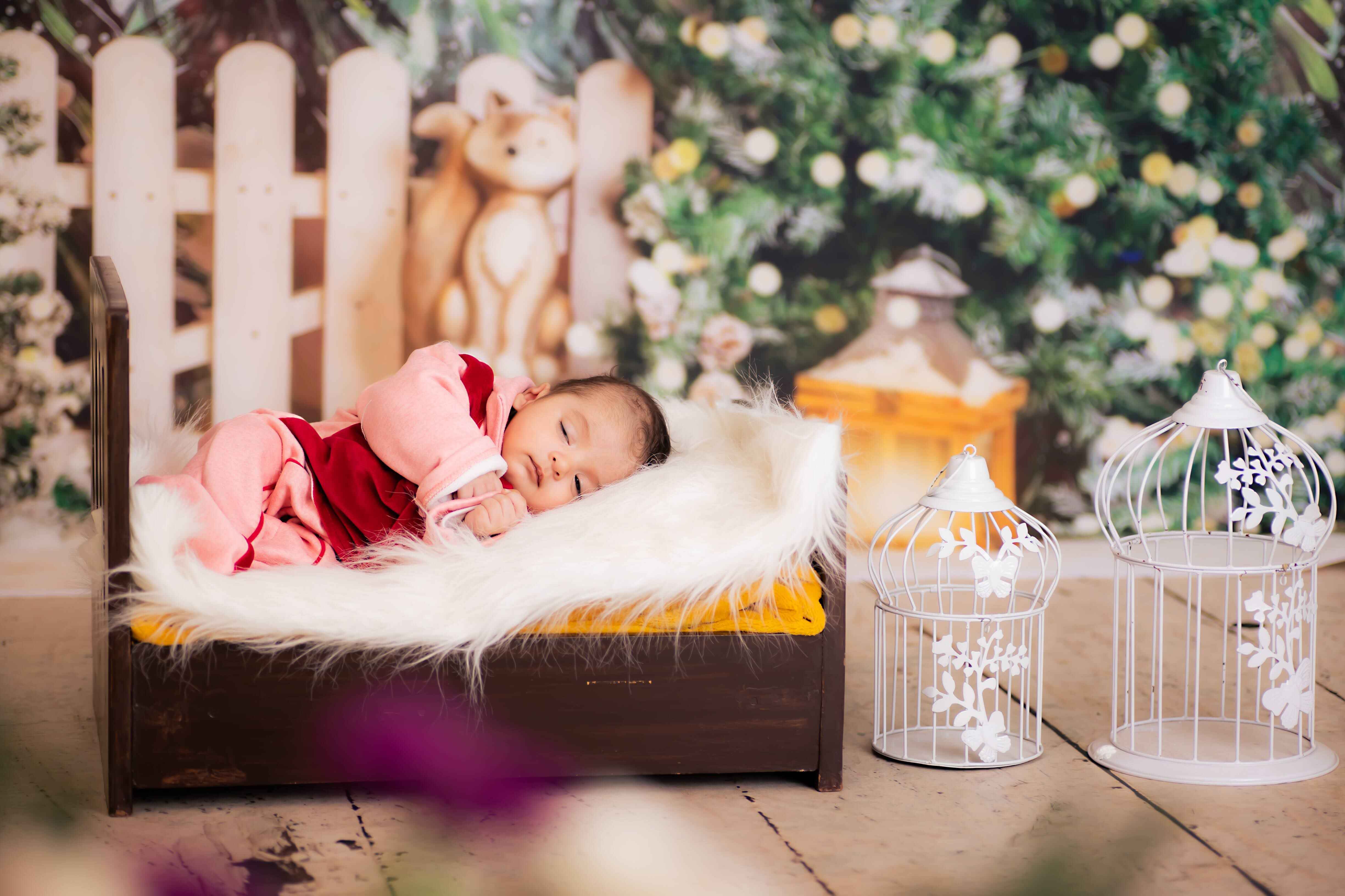 A baby lying in a white fur bed, with a Christmas tree and festive decorations in the background, captured in a joyful baby photoshoot.